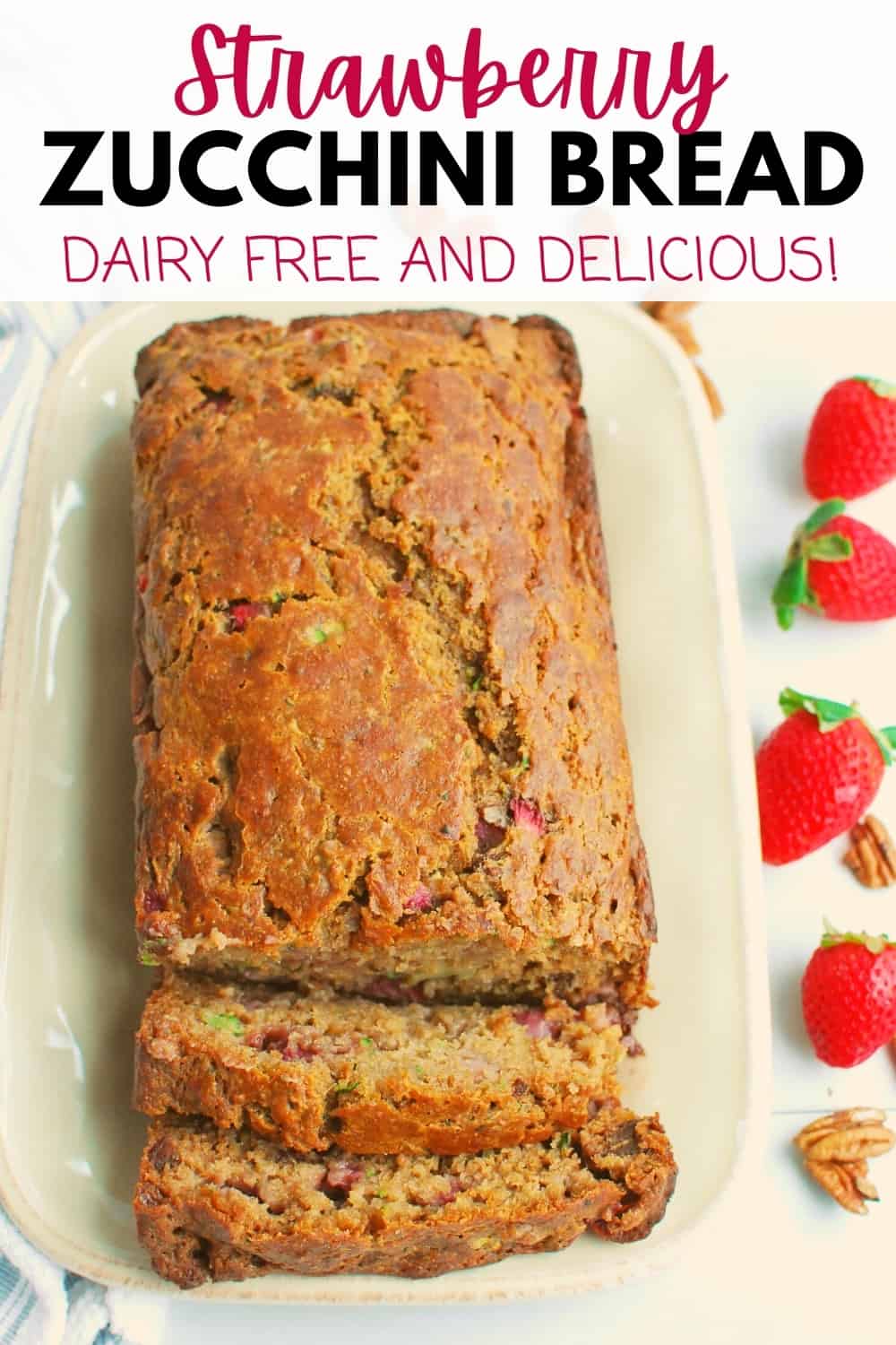 A loaf of strawberry zucchini bread on a rectangular plate next to some fresh strawberries.