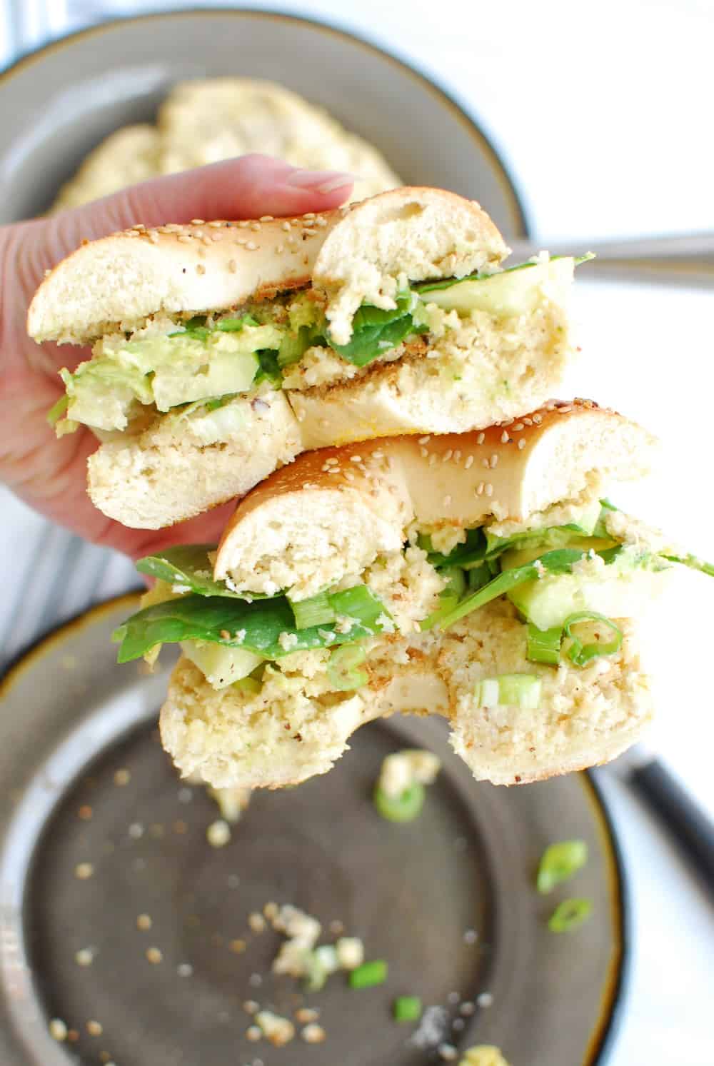 A woman's hand holding two halves of the bagel sandwich.