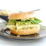 A vegan bagel sandwich on a grey plate with a bowl of dairy free cream cheese in the background.