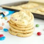 A stack of five dairy free M&M cookies next to some scattered candies and a baking sheet.