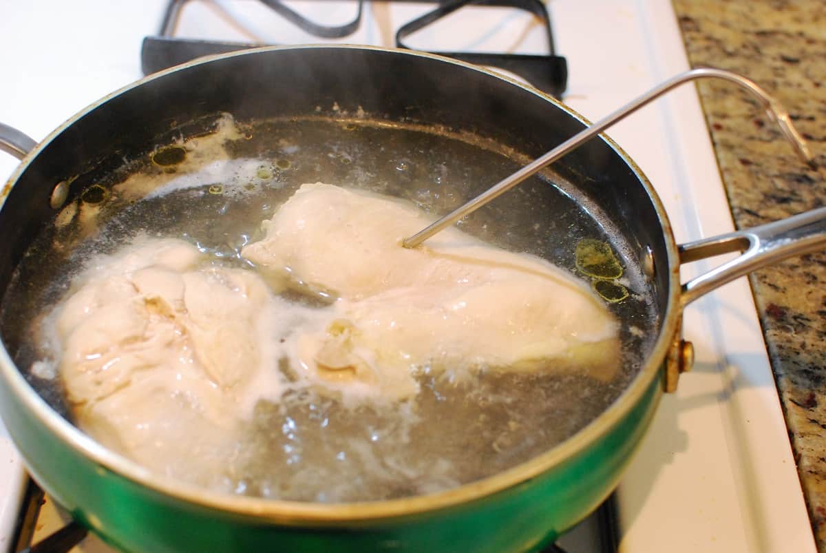 Chicken in a sauté pan simmering in water.
