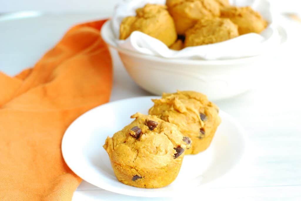 Pumpkin muffins with chocolate chips on a plate next to an orange napkin.