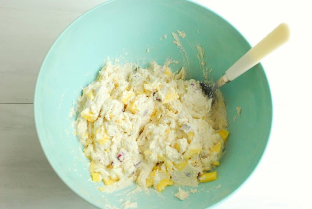 Cashew cream mixed with mango and red onion in a mixing bowl.