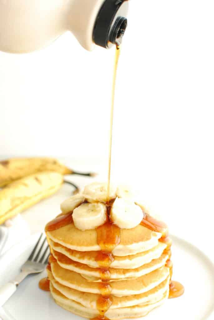 A bottle of maple syrup being poured on a stack of dairy free banana pancakes.