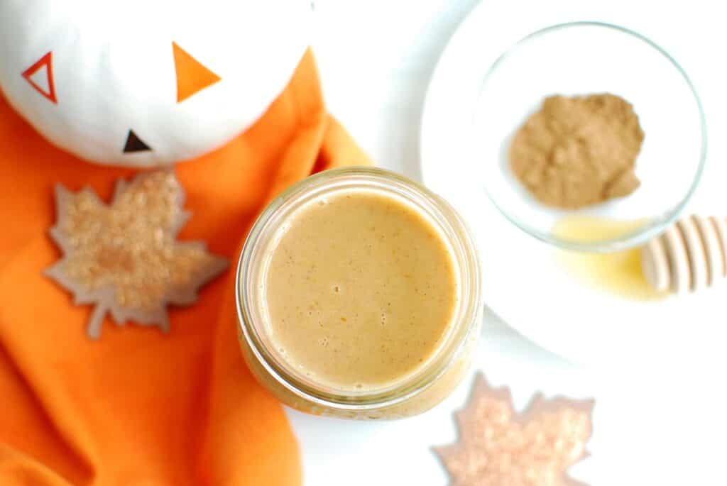 Overhead shot of a jar of pumpkin coffee creamer next to some pumpkin spice and honey.