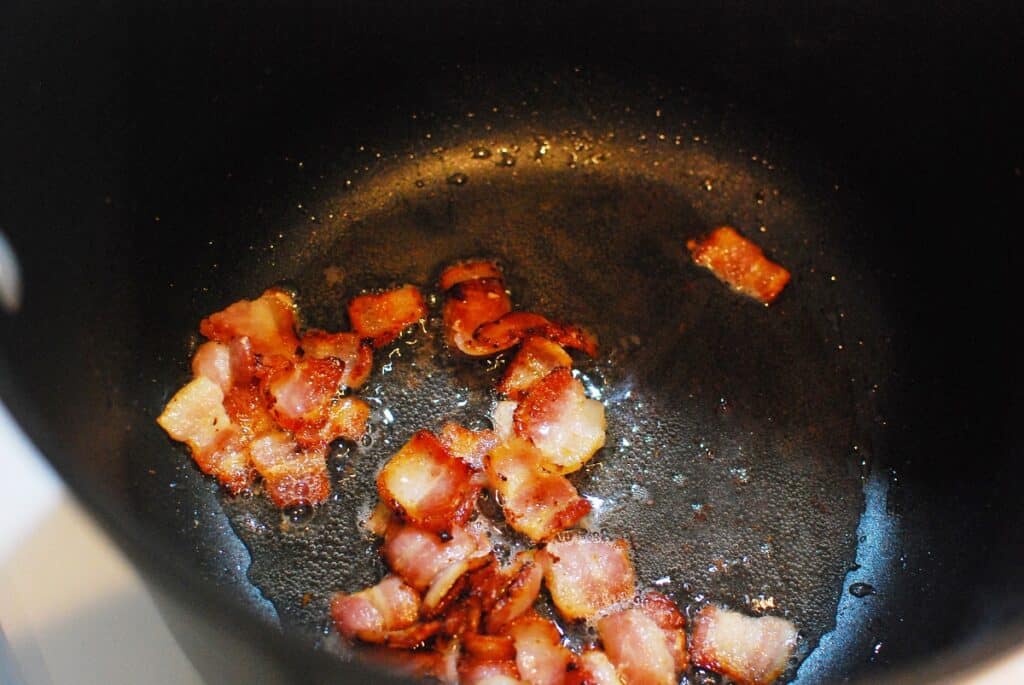 Chopped bacon cooking in a pot.