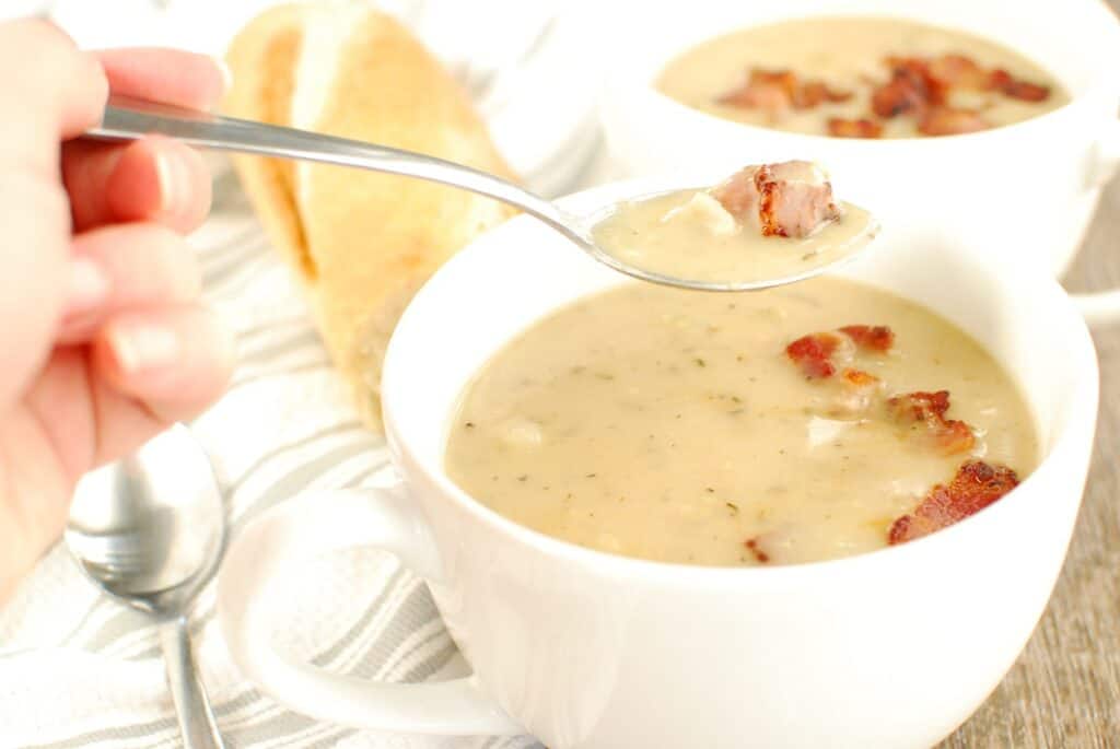 A woman taking a spoonful of dairy free clam chowder from a mug.