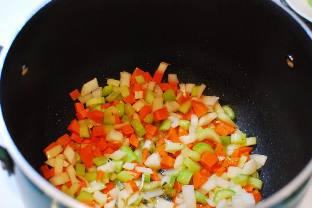 Celery, carrots, and onion being sautéed in bacon grease in a pot.