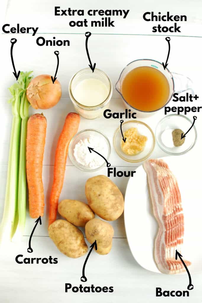 Ingredients on a table - celery, carrots, potatoes, onion, flour, garlic bacon, salt, pepper, oat milk, and chicken stock.