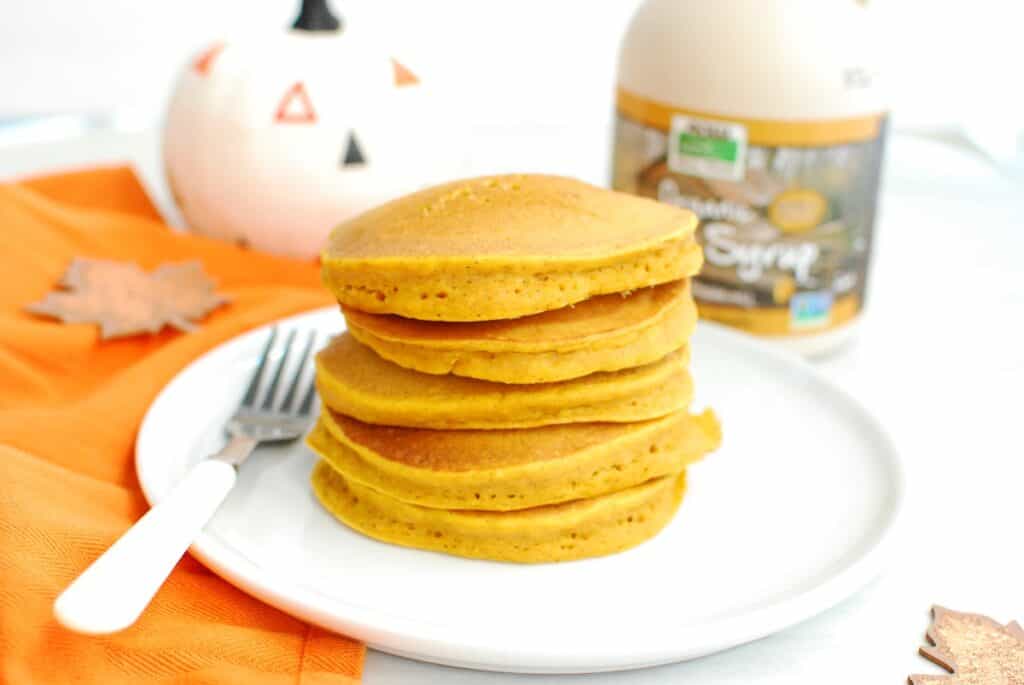 Dairy free pumpkin pancakes on a white plate next to a fork and napkin.