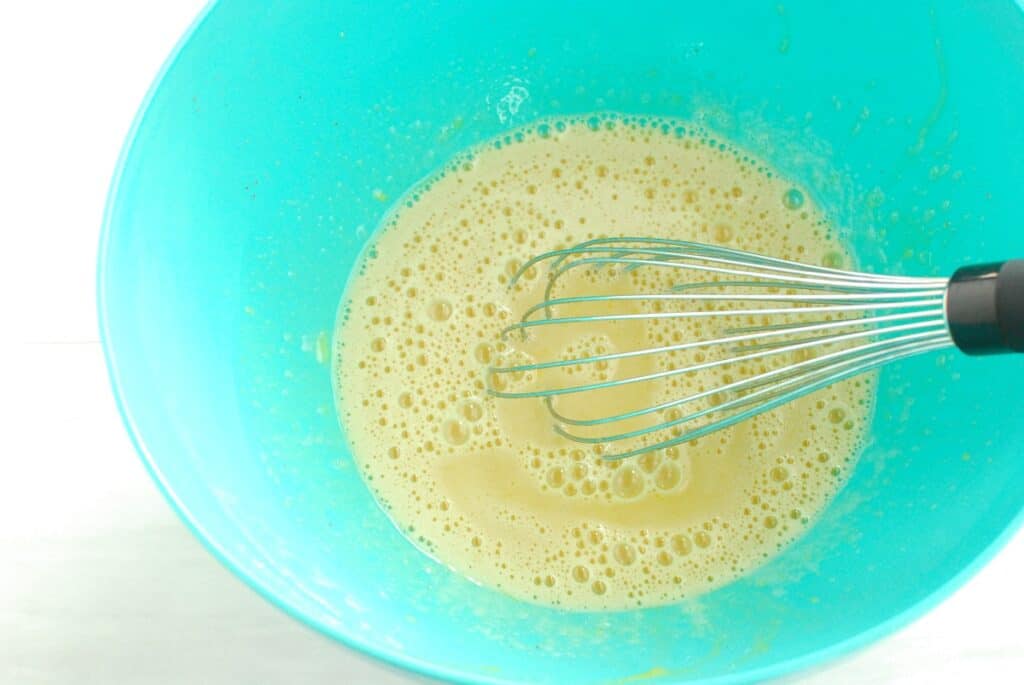 Tempering the eggs by whisking the hot oat milk mixture into the bowl with the egg yolks.