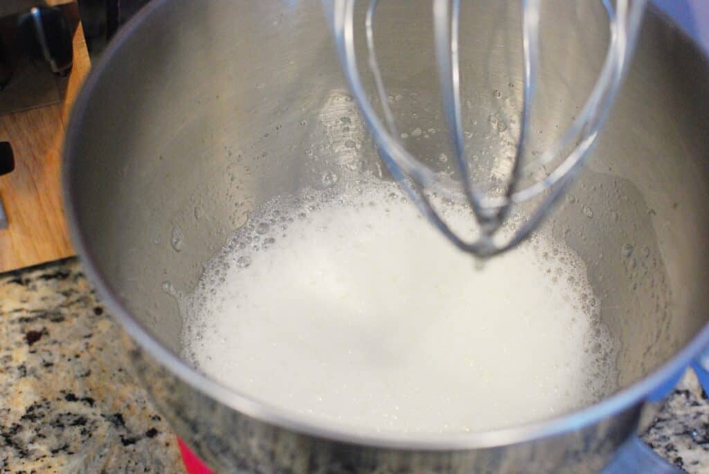 Foamy egg whites in a mixing bowl under a stand mixer.