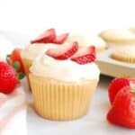 An angel food cupcake topped with frosting and sliced strawberries.