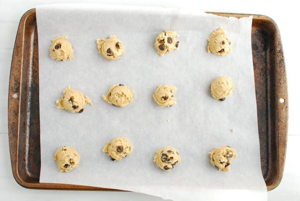 Scoops of cookie dough portioned out on a parchment-lined baking sheet.