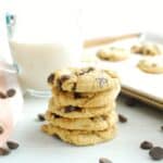 Several dairy free cookies stacked on each other, with a glass of oat milk in the background.