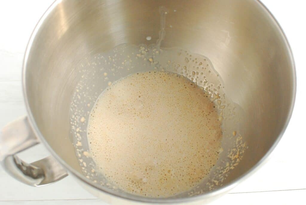 Yeast mixed with sugar and warm oat milk in a mixing bowl.