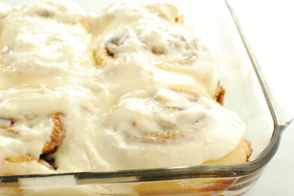 Frosting spread on top of cinnamon rolls in a baking dish.