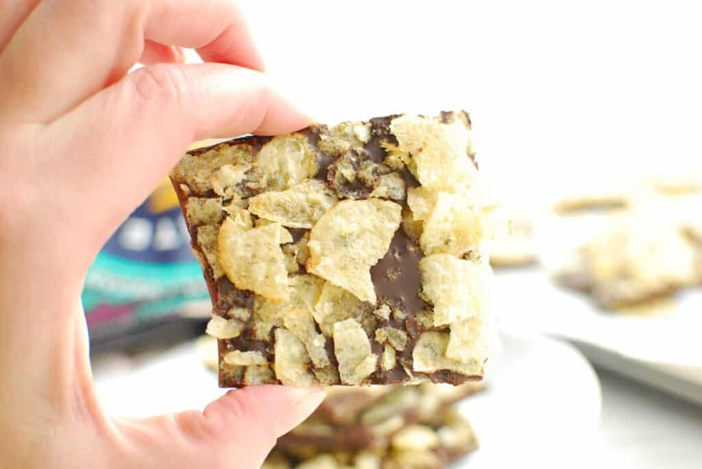 A woman's hand holding a piece of dark chocolate potato chip bark.