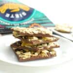 Dark chocolate potato chip bark stacked on top of each other, with a bag of potato chips in the background.