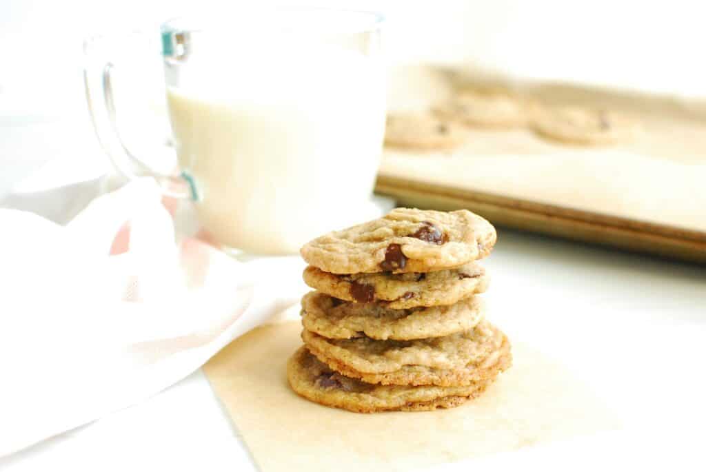 A stack of coconut oil chocolate chip cookies next to a glass of oat milk.