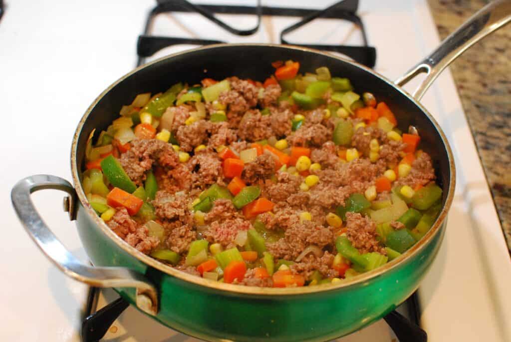 Beef browning with vegetables in a sauté pan.