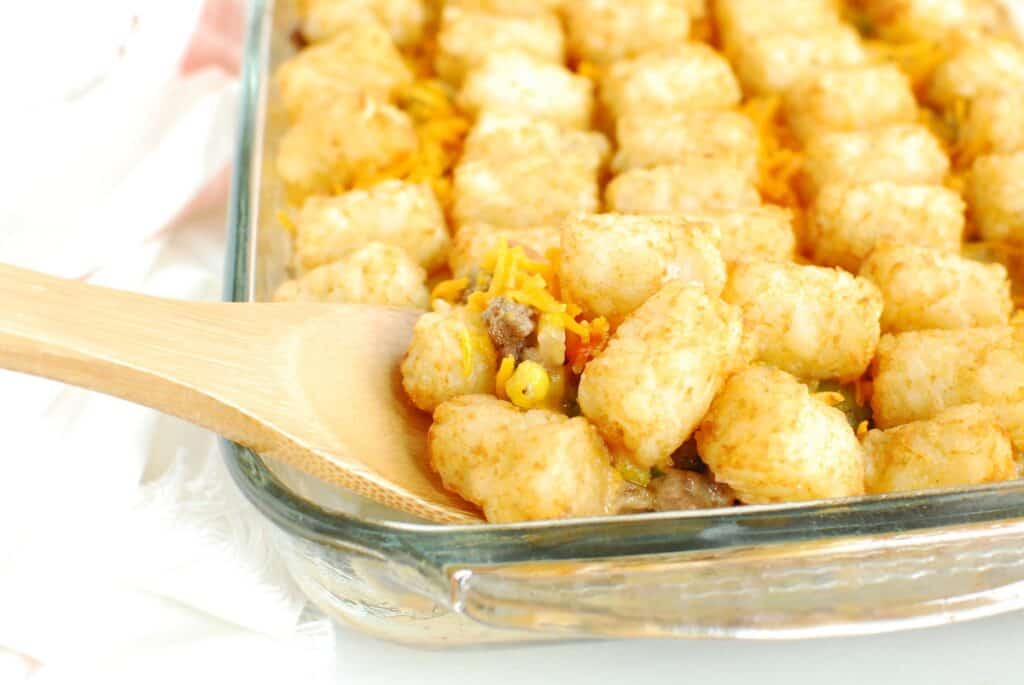 A wooden spoon scooping out dairy free tator tot casserole from a glass dish.