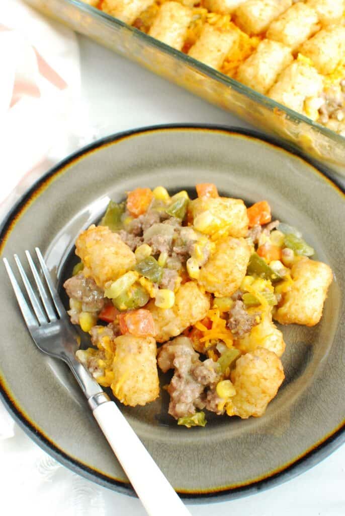 A plate with a heaping scoop of dairy free tator tot casserole on it, with a fork on the edge.