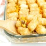 A wooden spoon scooping out dairy free tator tot casserole from a glass dish.