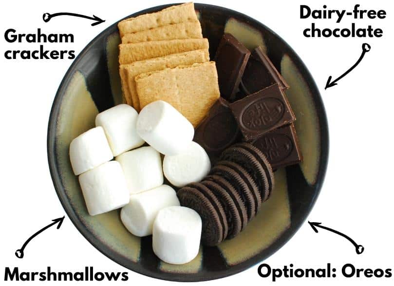 A bowl with marshmallows, graham crackers, chocolate, and oreo cookies.