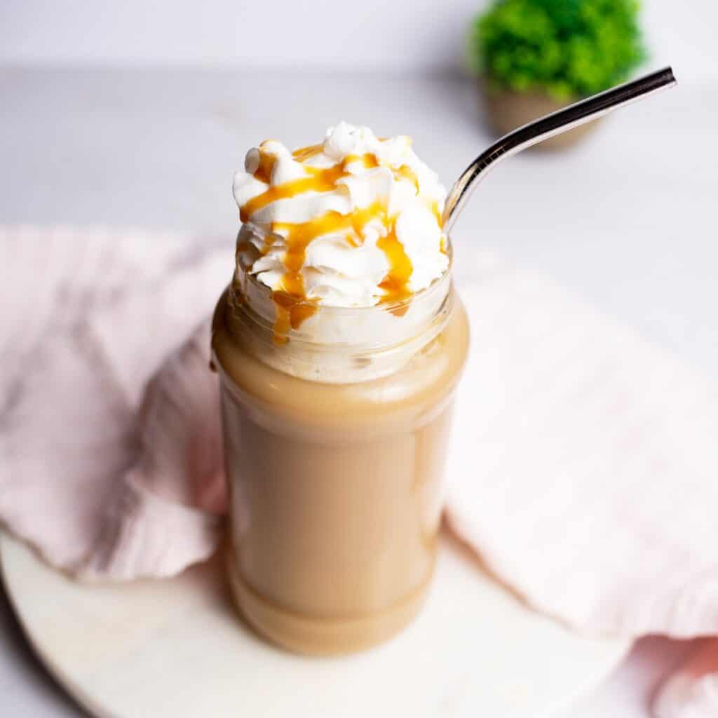 Dairy free oat milk caramel latte in a glass with a metal straw next to a napkin.