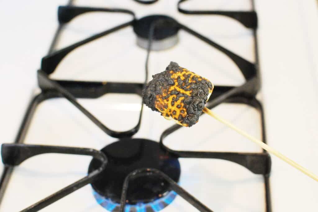 A marshmallow being roasted over a gas stove.