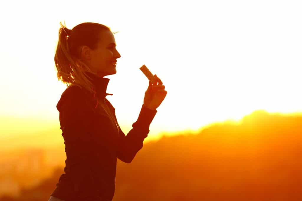 A woman eating a high protein dairy free snack outside after a workout at sunset.