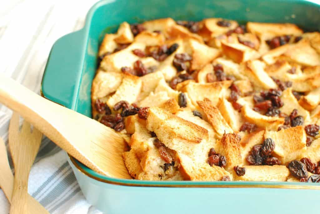 A wooden spoon scooping up some dairy free bread pudding from a baking dish.