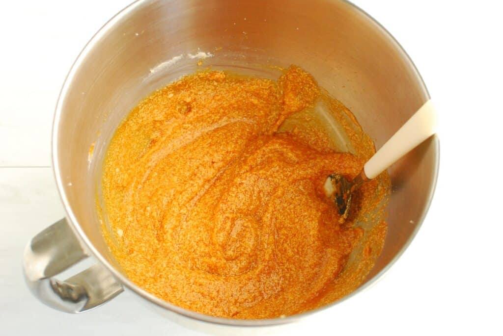 Butter, sugar, egg, vanilla, and pumpkin mixed together in a bowl.