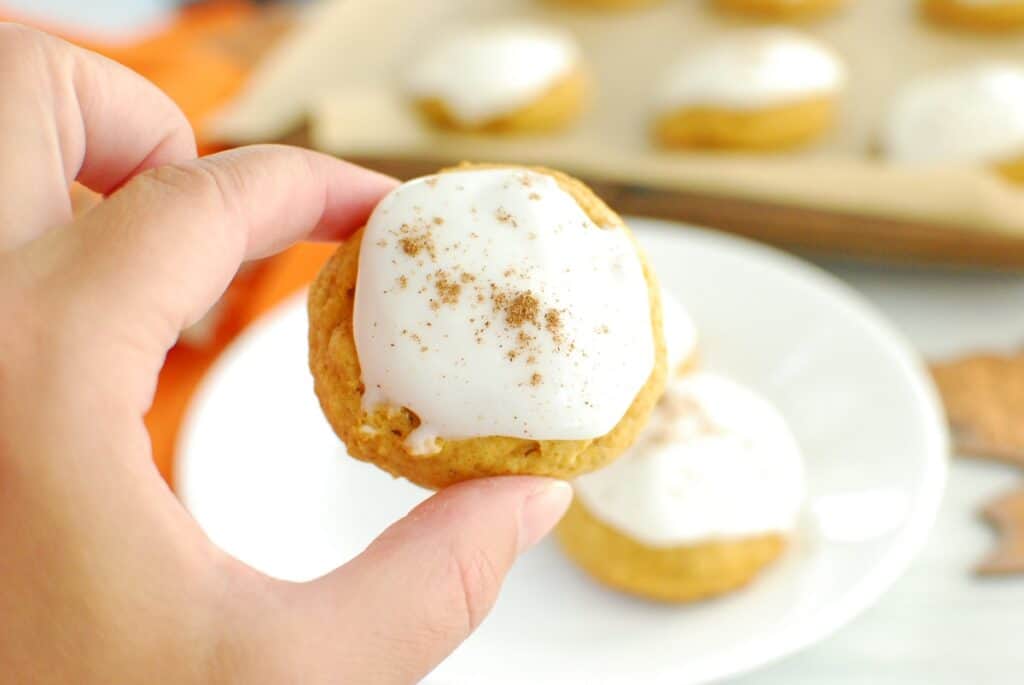 A woman's hand holding a dairy free pumpkin cookie with frosting.