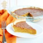 A slice of dairy free pumpkin pie on a white plate next to an orange napkin and a fork.