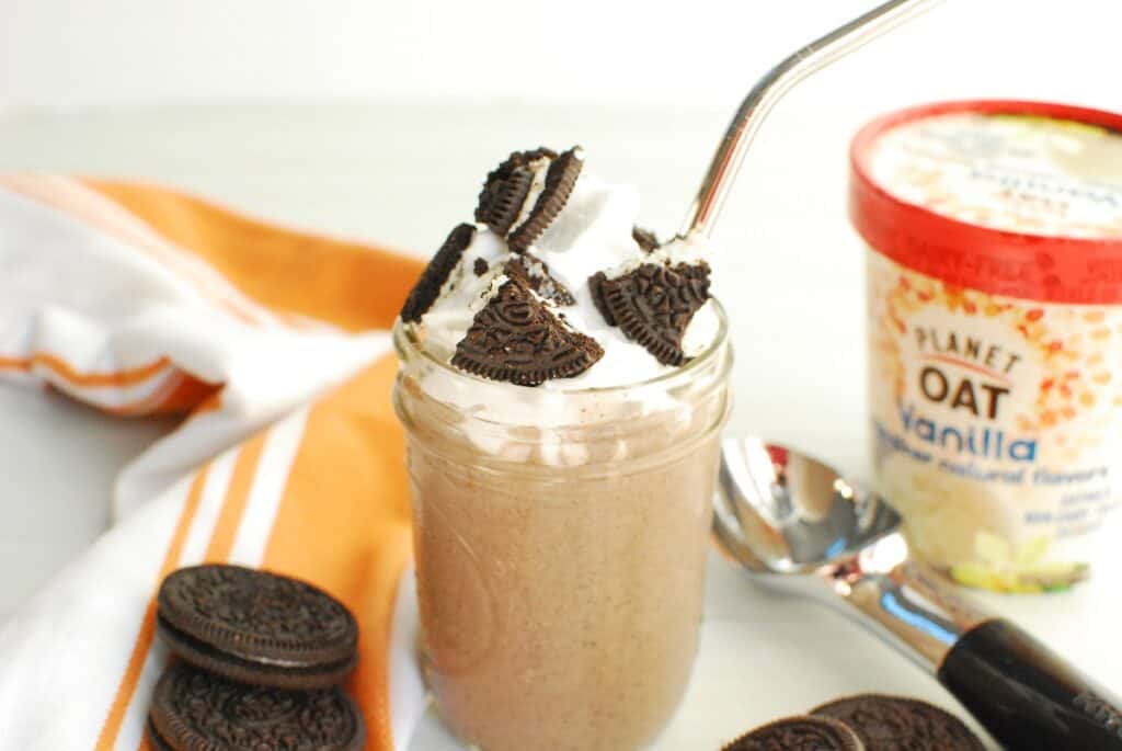A dairy free cookies and cream milkshake topped with whipped cream and oreos.