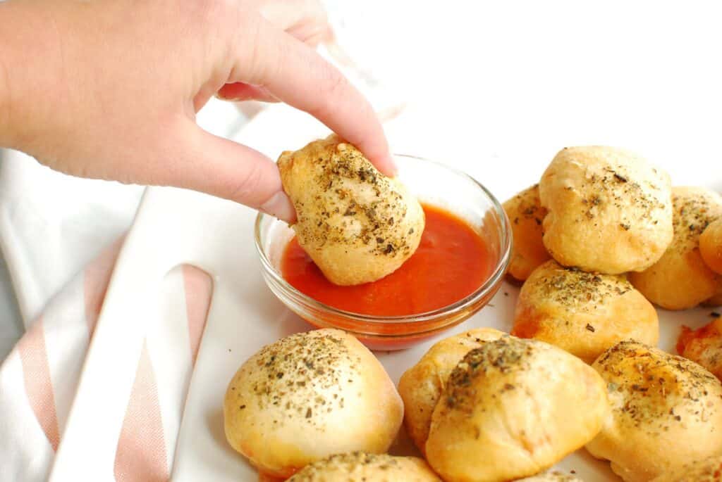 A woman dipping a pizza bomb into marinara sauce.