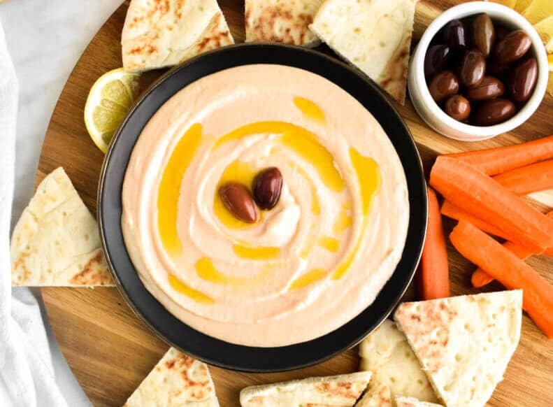 Taramosalata dip in a bowl next to pita, carrots, and olives.