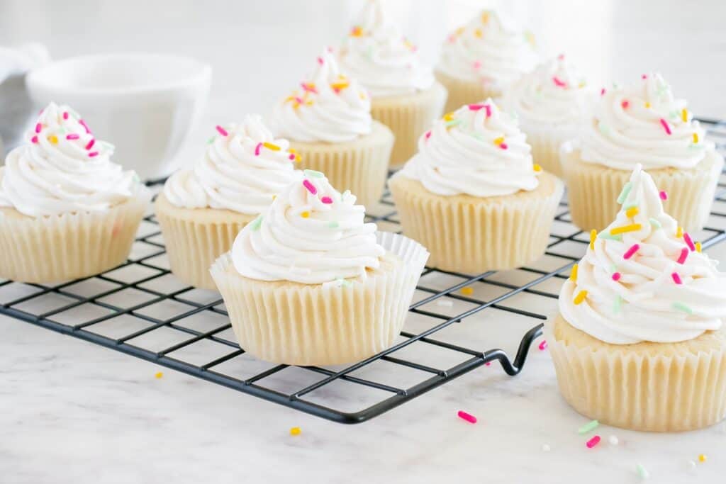 A bunch of cupcakes topped on a cooling rack topped with dairy free vanilla buttercream.