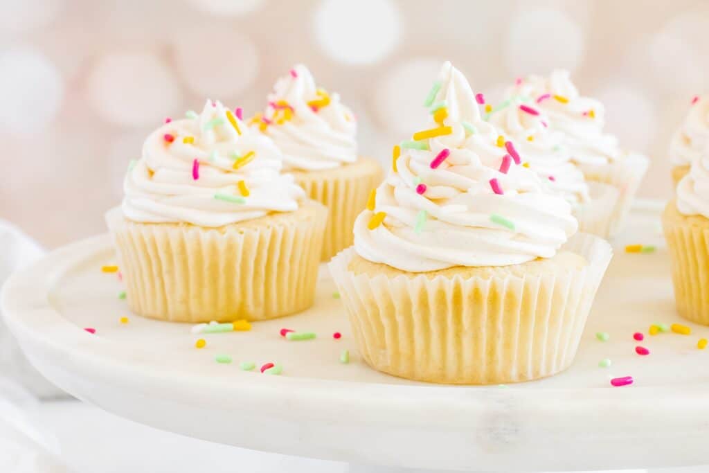 Several dairy free vanilla cupcakes topped with frosting and sprinkles.