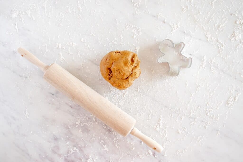 A ball of gingerbread cookie dough next to a rolling pin and cookie cutter.