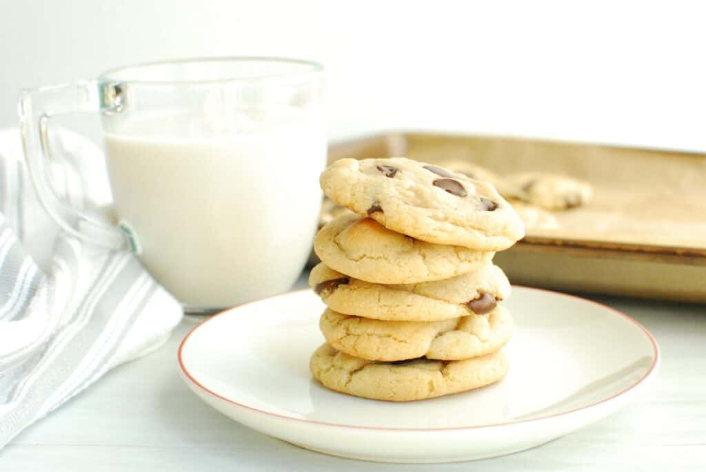 A stack of no butter chocolate chip cookies on a plate next to a glass of almond milk.