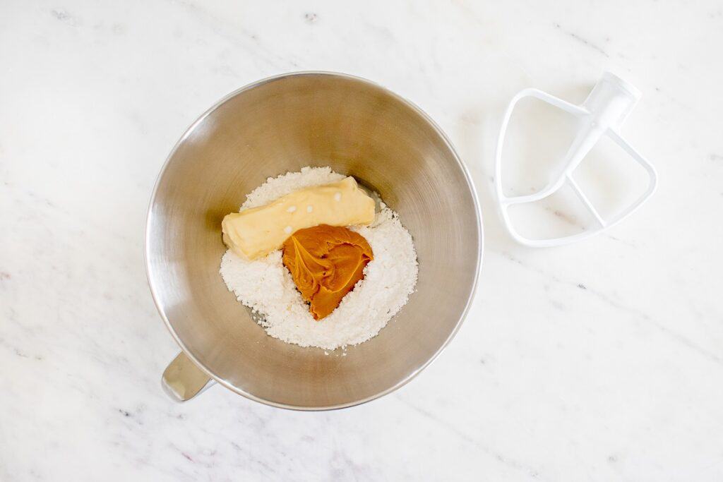 Powdered sugar, dairy free butter, peanut butter, dairy free milk, and vanilla added to a stand mixer bowl.