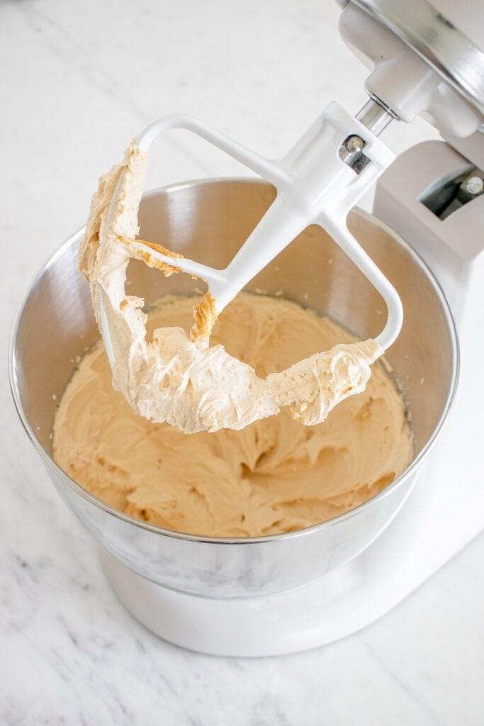 Dairy free peanut butter frosting in a stand mixer bowl, with some frosting on the attachment.