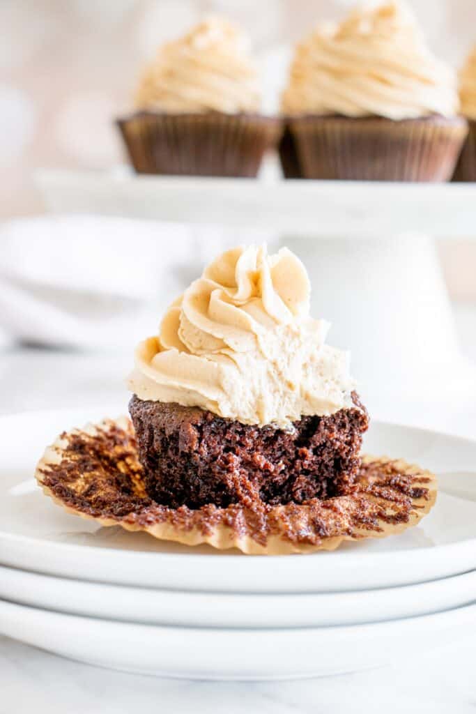 A peanut butter frosted cupcake with a bite taken out of it on a white plate.