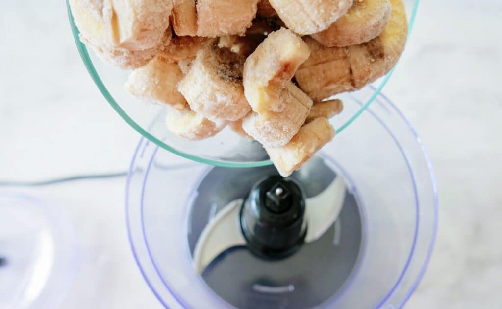 Pouring frozen banana chunks into a food processor bowl.