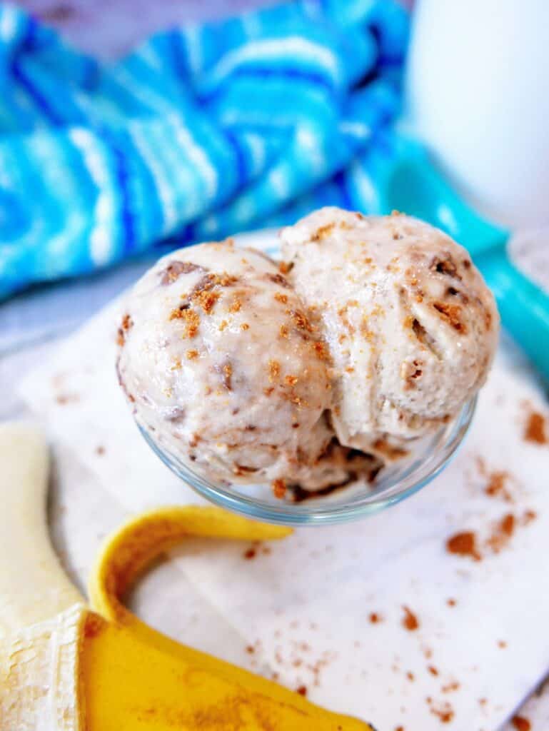 A glass bowl with banana nice cream next to a banana and a napkin.