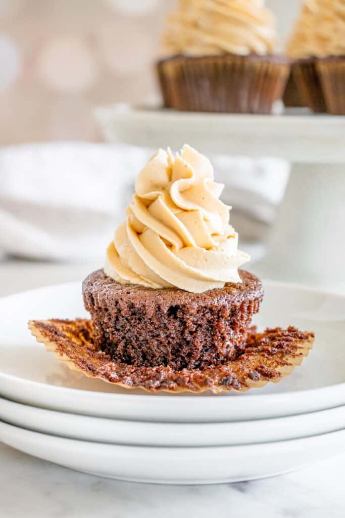 A dairy free chocolate cupcake with the liner peeled down on a white plate.