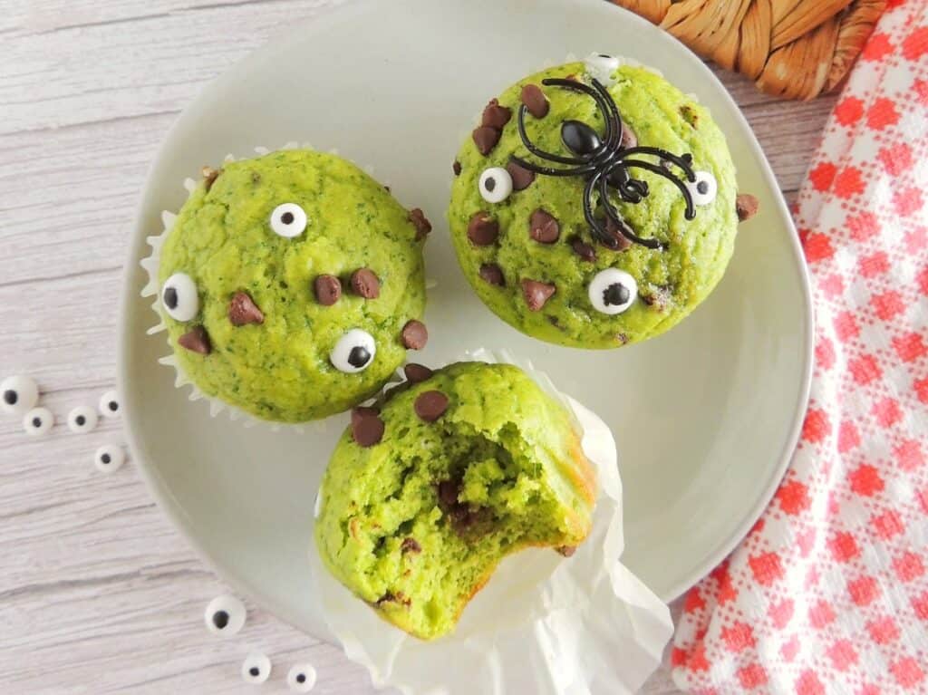 Three Halloween monster muffins on a white plate next to a napkin and some googly eyes.